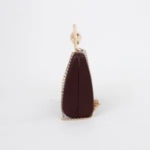 Side profile detail of the burgundy hard-shell evening clutch with gold chain strap.