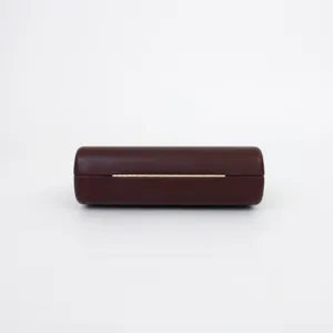 Close-up detail of the cylindrical evening bag in deep burgundy with gold hinge hardware.