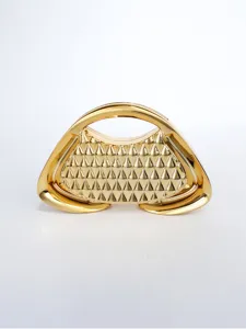 Dettaglio della borsa rigida dorata con forma trapezoidale geometrica e finitura con borchie.