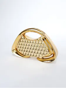 Dettaglio clutch rigida metallica dorata, forma trapezoidale geometrica e borchie uniche.