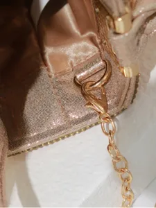 Close-up detail of metallic evening bag featuring sparkling fabric, gold chain strap, and refined hardware.