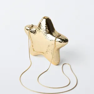 Metallic star-shaped evening clutch bag detail, shiny gold metal finish with slim chain.