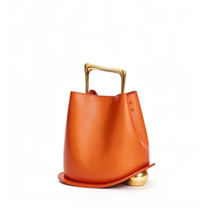 Orange leather bucket bag with unique gold metal handle and spherical base for women stylish design.