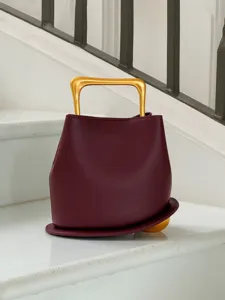 Burgundy leather bucket bag detail featuring a unique rigid gold handle and curved base design.