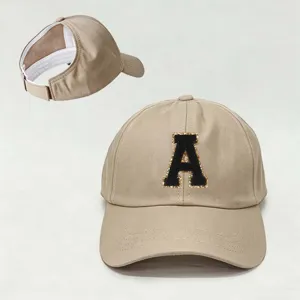 Detalle gorra de béisbol caqui, parche letra A negra, abertura cola de caballo, correa ajustable.