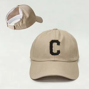 Vista detallada de la gorra de béisbol beige para coleta con parche de letra negra ajustable.