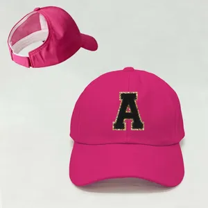 Detalle de la gorra rosa de cola de caballo con parche de letra A con brillo negro.