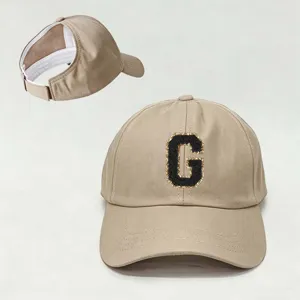 Vista detallada de la gorra de béisbol beige con parche de letra negra y correa ajustable.