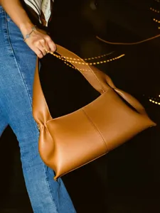 Detail shot of brown leather hobo shoulder bag, dumpling shape with long handle, niche style.