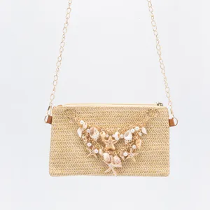 Detailed view of straw woven shoulder bag featuring gold chain, seashell and pearl decorations.