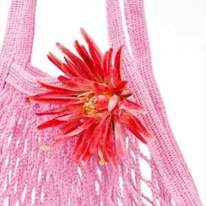 Detail of pink crochet mesh tote bag, knit beach bag texture, red flower decoration closeup.
