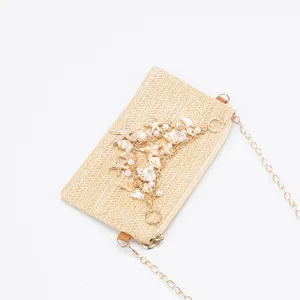Straw shoulder bag detail featuring seashell, pearl, and starfish charms with gold chain.