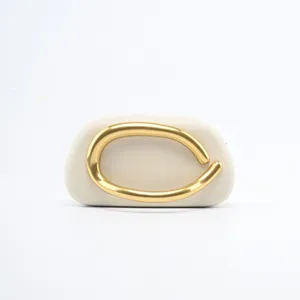 Elegant minimalist gold metal handle abstract clutch bag detail shot on clean white.