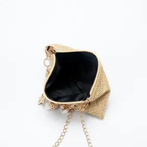 Detail shot of straw woven shoulder bag featuring shell, pearl and gold chain decoration.