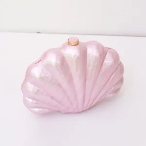 Close-up of pink acrylic shell clutch bag showing pearlescent texture and golden clasp detail.