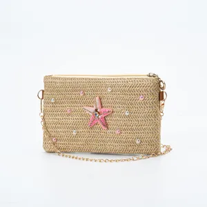 Close-up view of the straw woven crossbody bag featuring a pink beaded starfish and pearls.
