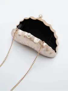 Detailed closeup of the shell-shaped acrylic clutch bag featuring a pearl clasp and gold chain.