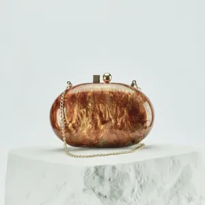 Elegant oval acrylic evening clutch bag with gold chain strap and marbled glitter finish.