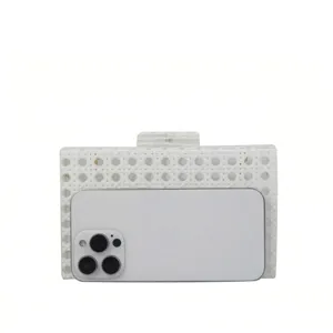 Detail view of a white woven rattan and acrylic clutch handbag, showcasing size with a phone.