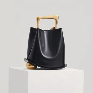 Stylish black leather bucket bag featuring gold sculptural handle and modern luxury daily accessory.