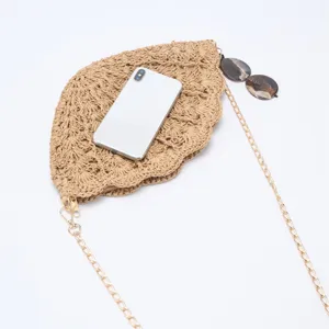 Detailed view of a fashionable hollow straw shell cross-body bag with golden chain for beach.