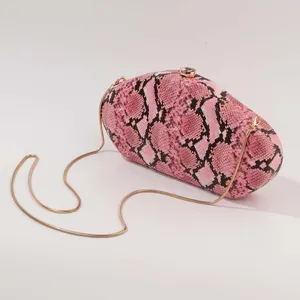 Gros plan sur le sac clutch de soirée en acrylique imprimé serpent rose chaîne dorée.