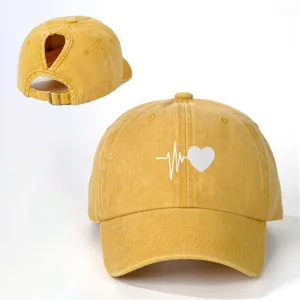 Washed yellow ponytail baseball cap with white heart heartbeat graphic and adjustable back strap.