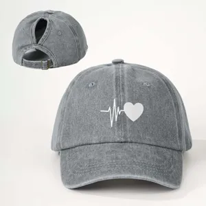 Detailed view of grey washed denim baseball cap with ponytail hole and heart beat print.
