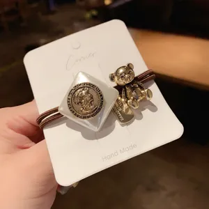 Detailed close-up of retro metal bear and coin charm hair tie on a white display card.