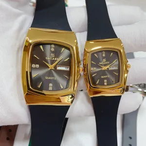 GALAXY koppel quartz horloge met gouden gebogen kast, zwarte siliconen band en datumweergave.