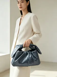 Detailed view of the dark grey gathered clutch bag held elegantly by a model indoors.