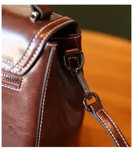 Detailed view of brown leather vintage crossbody bag with contrast stitching and metal hardware.