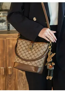 Detailed shot of luxury monogram bucket bag with metal lock and cute rabbit keychain pendant.