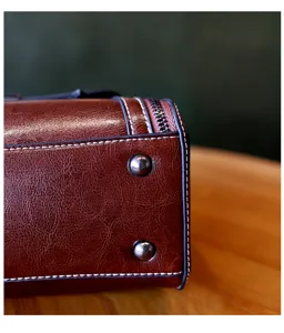 Close-up detail of retro brown leather handbag showing fine stitching, metal feet and side zipper.