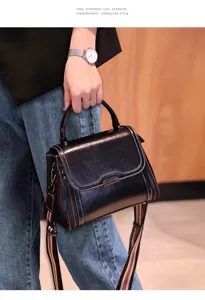 Detailed close-up view of black leather top-handle crossbody bag with striped strap.