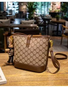 Brown monogram bucket bag featuring plush rabbit pendant and stylish leather crossbody strap.