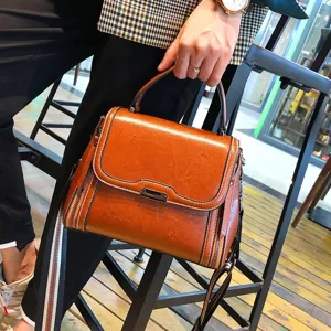 Brown leather handbag detail shot showing premium texture, stitching and metallic lock clasp.