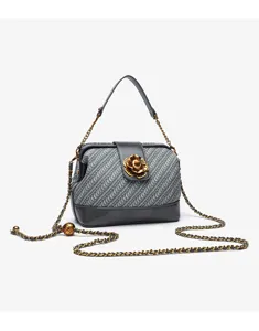 Detailed close-up of the woven shell handbag featuring an elegant golden camellia flower clasp and chain strap.
