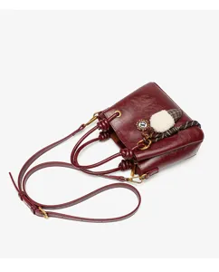 Dark red retro bucket bag detail showing knotted handle, leather texture, and cute plush charm.