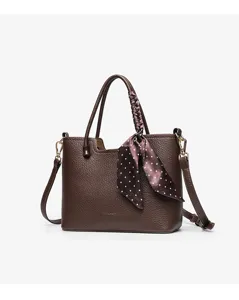 Close-up detail of the brown leather tote bag showing fine texture and silk polka dot scarf.