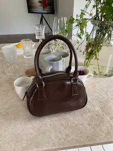 Close-up detail of dark brown patent bowling handbag, classic glossy finish and zipper.