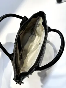 Interior detail view of a black leather handbag showing light patterned lining and zipper pocket.