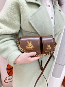 Brown leather shoulder bag detailed with stylish gold chain and unique metal rabbit head decor.
