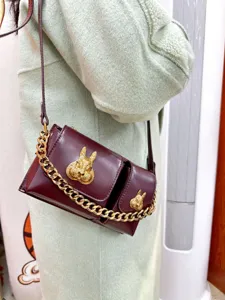 Maroon leather cross-body bag detail, featuring gold rabbit hardware and chic chain accent.
