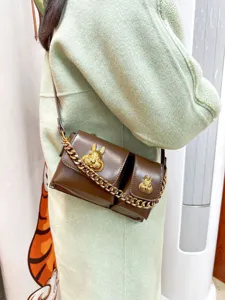 Detail view of brown leather crossbody motorcycle bag with gold rabbit hardware and chains.