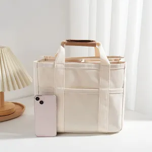 Close-up view of a multi-compartment canvas storage tote bag with brown leather handles.