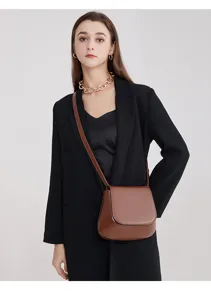Detailed shot of a stylish brown leather saddle bag worn crossbody by a model in black blazer.