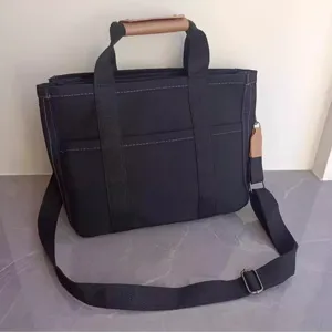 Black canvas tote bag detail, featuring durable webbed handles and brown leather grip.
