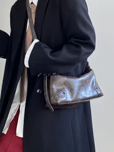 Detailed close-up of a vintage brown distressed leather underarm shoulder bag with metal eyelets.
