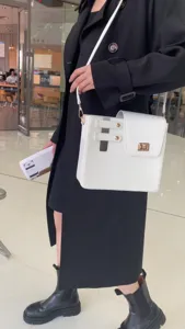 Minimalist white shoulder bag detail shot worn by model in elegant black trench coat.